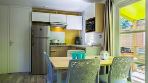 Uma cozinha compacta com geladeira, fogão e micro-ondas. Há uma área de refeições com mesa e cadeiras.
