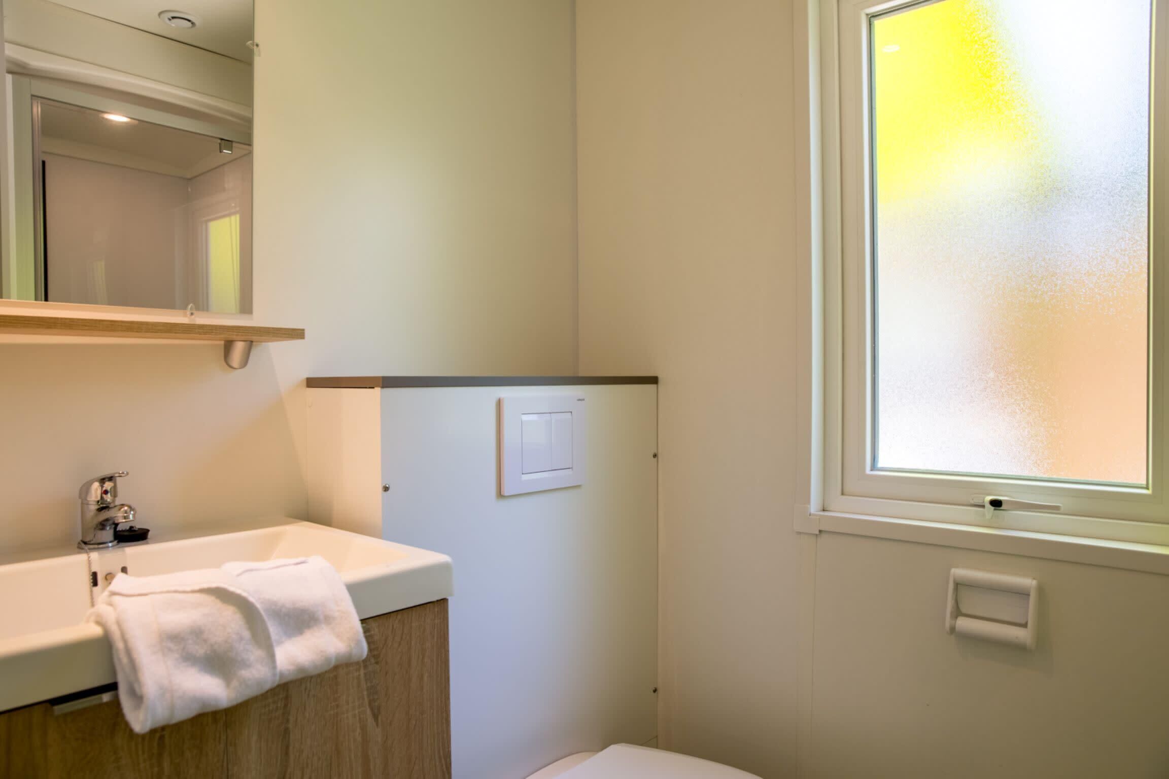 A bathroom with a white sink, a towel, a mirror, a light switch, and a frosted window.