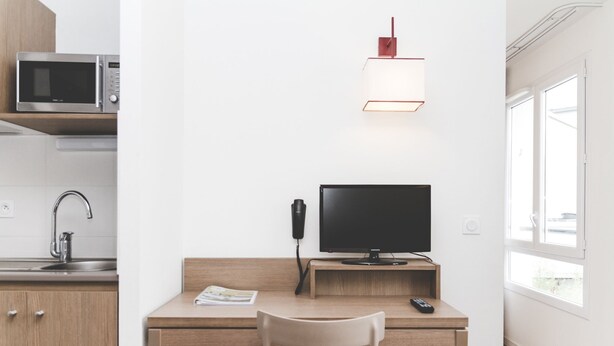 Een moderne keuken met een magnetron, een spoelbak en een houten bureau met een computer en een afstandsbediening.