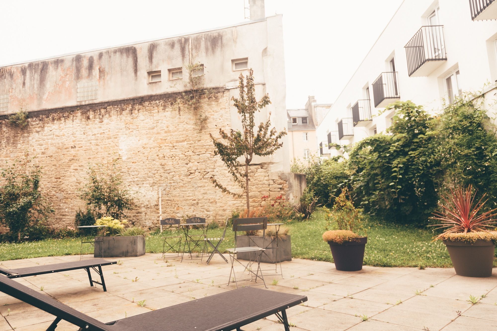 Une cour intérieure avec un mur en pierre, un petit arbre, du mobilier d’extérieur et des plantes en pot.