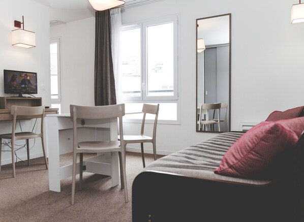 Una habitación de hotel moderna con una cama, un escritorio con sillas, un televisor y un espejo grande.