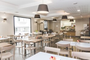 Un comedor amplio con varias mesas y sillas, ventanas grandes e iluminación colgante.