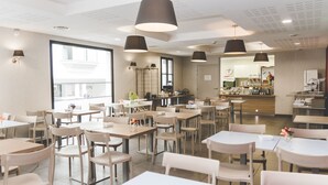 Un comedor amplio con varias mesas y sillas, ventanas grandes e iluminación colgante.