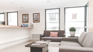 Una sala de estar moderna con un sofá, una mesa de centro y una chimenea. Hay cuadros enmarcados en la pared y una ventana con vistas al exterior.