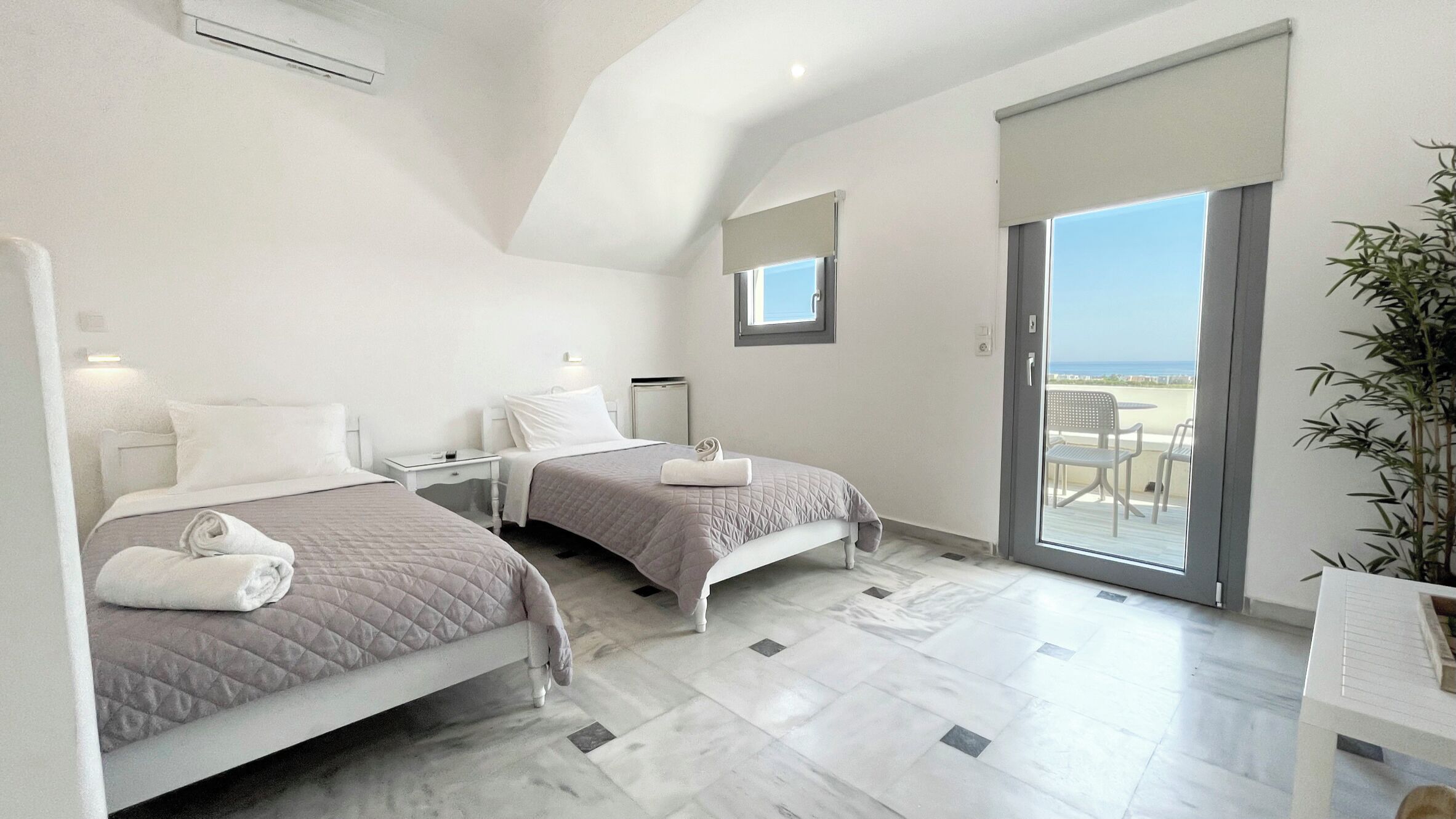 A hotel room with two beds, a balcony with a view, and a small table.