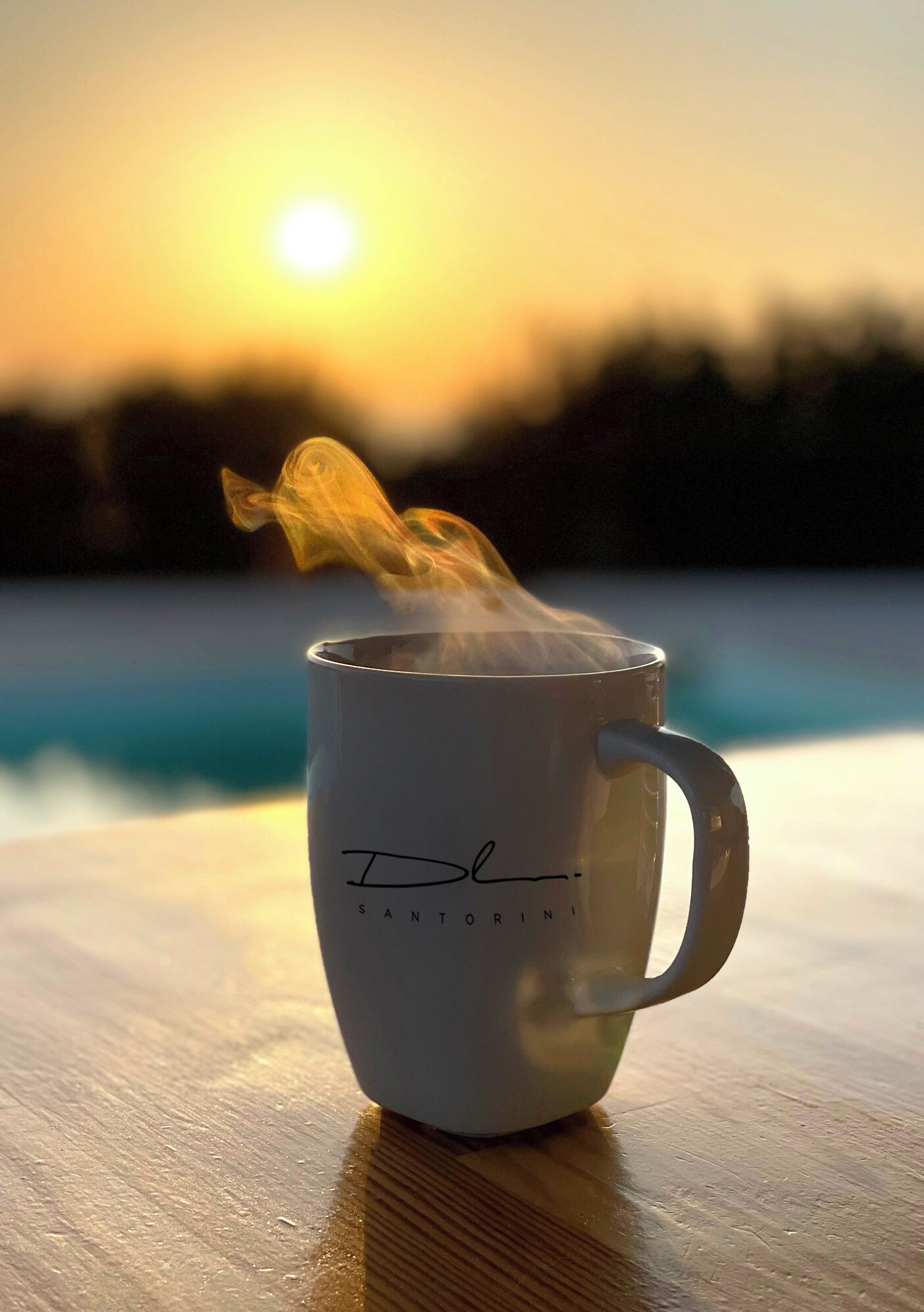 Una taza blanca con vapor saliendo, sobre una superficie de madera, con un fondo desenfocado de un cuerpo de agua y un atardecer.