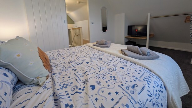 A bedroom with a bed, a TV, a wardrobe, and a ceiling light. - Digby house flat 2 (West Mersea)