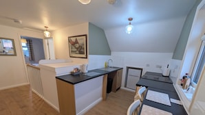 A compact kitchen with a small island, a refrigerator, and a dining area with a table and chairs. - Digby house flat 2 (West Mersea)