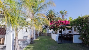 A well-maintained garden with a patio area, including a table and chairs, surrounded by various plants and a white wall. - 2stay-Aparments (Cape Town)