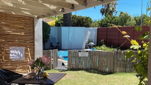 A patio area with a table and chairs, a pool, and a wooden fence with a notice sign. - 2stay-Aparments (Cape Town)