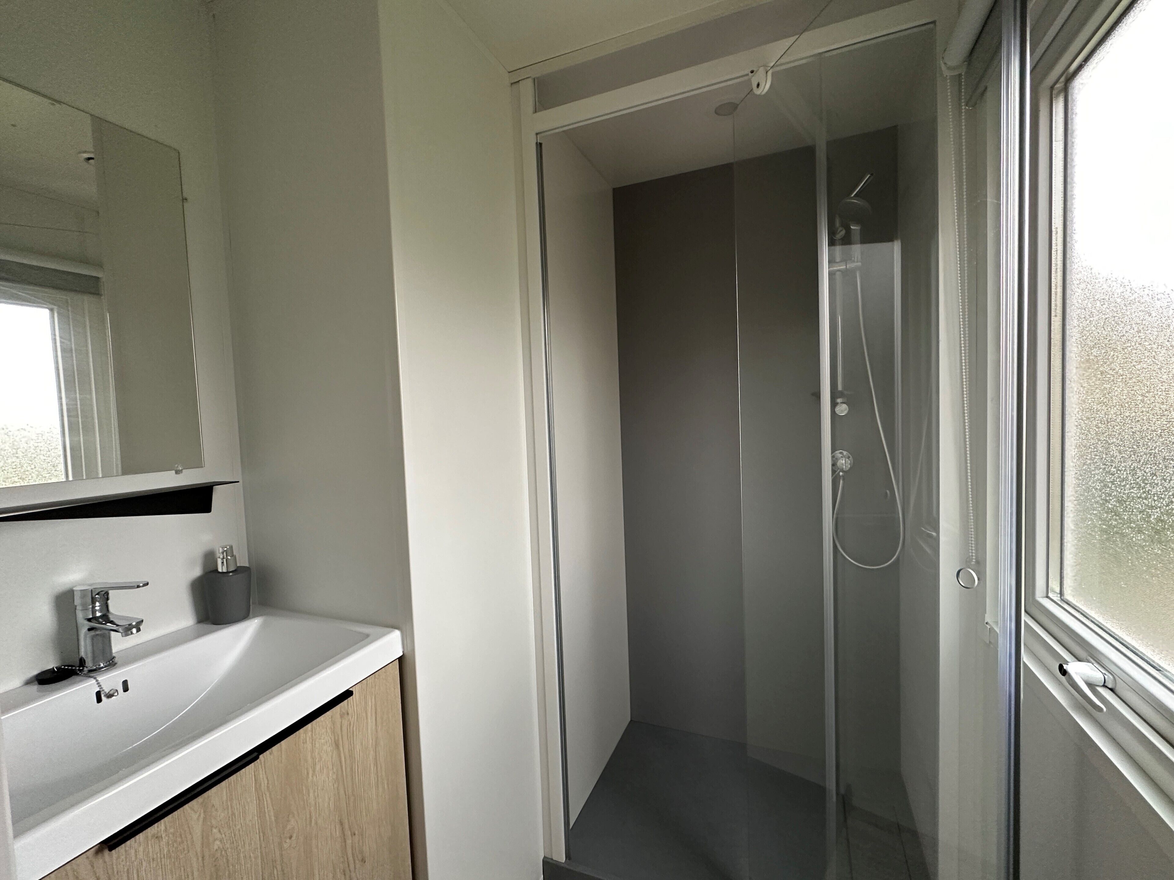 Un baño moderno con cabina de ducha de vidrio, un lavamanos blanco y un espejo sobre él.