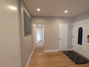 Un couloir doté d’un plancher en bois, de murs blancs et d’une porte ornée d’un panneau de verre décoratif.