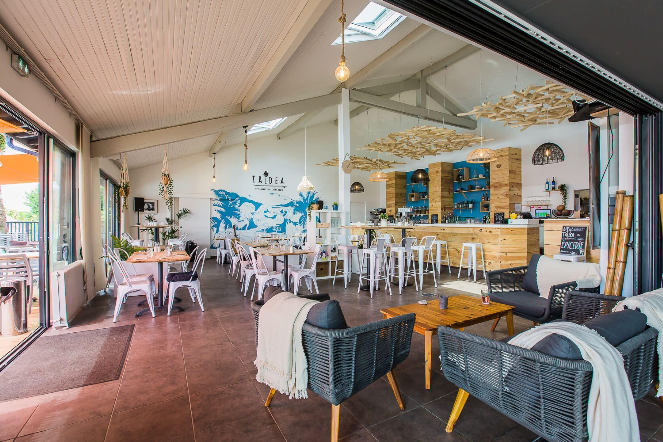 A restaurant with a bar area, white chairs, wicker furniture, and a mural on the wall.