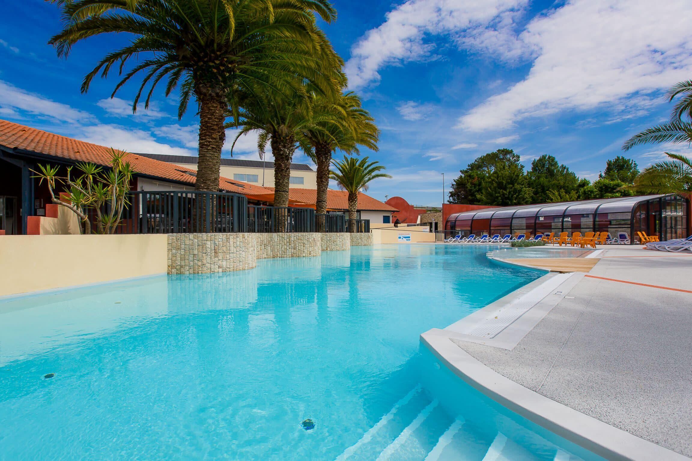 A swimming pool with clear blue water, surrounded by palm trees and lounge chairs.