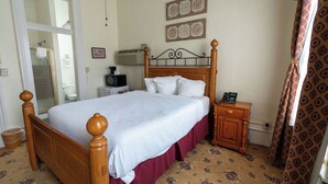 A bedroom with a wooden bed, a nightstand, a bedside table, a mirror, and a door leading to a bathroom.
