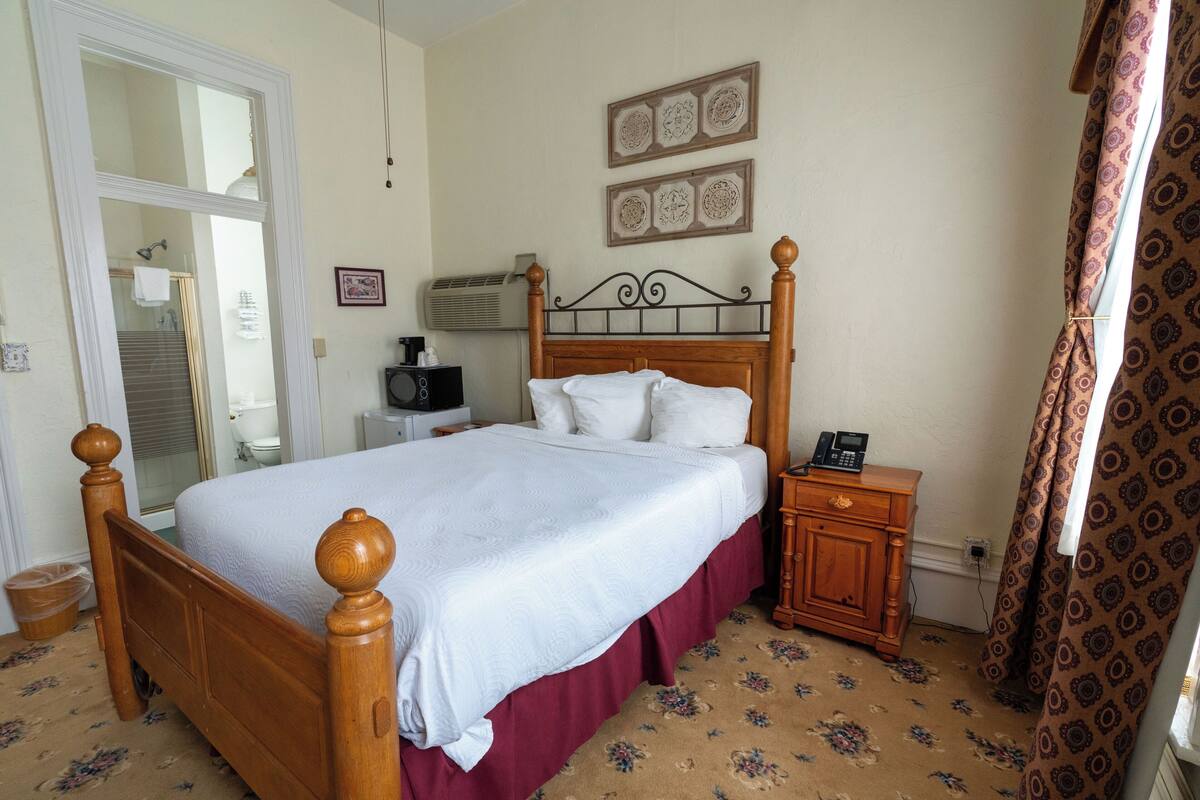 A bedroom with a wooden bed, a nightstand, a bedside table, a mirror, and a door leading to a bathroom.
