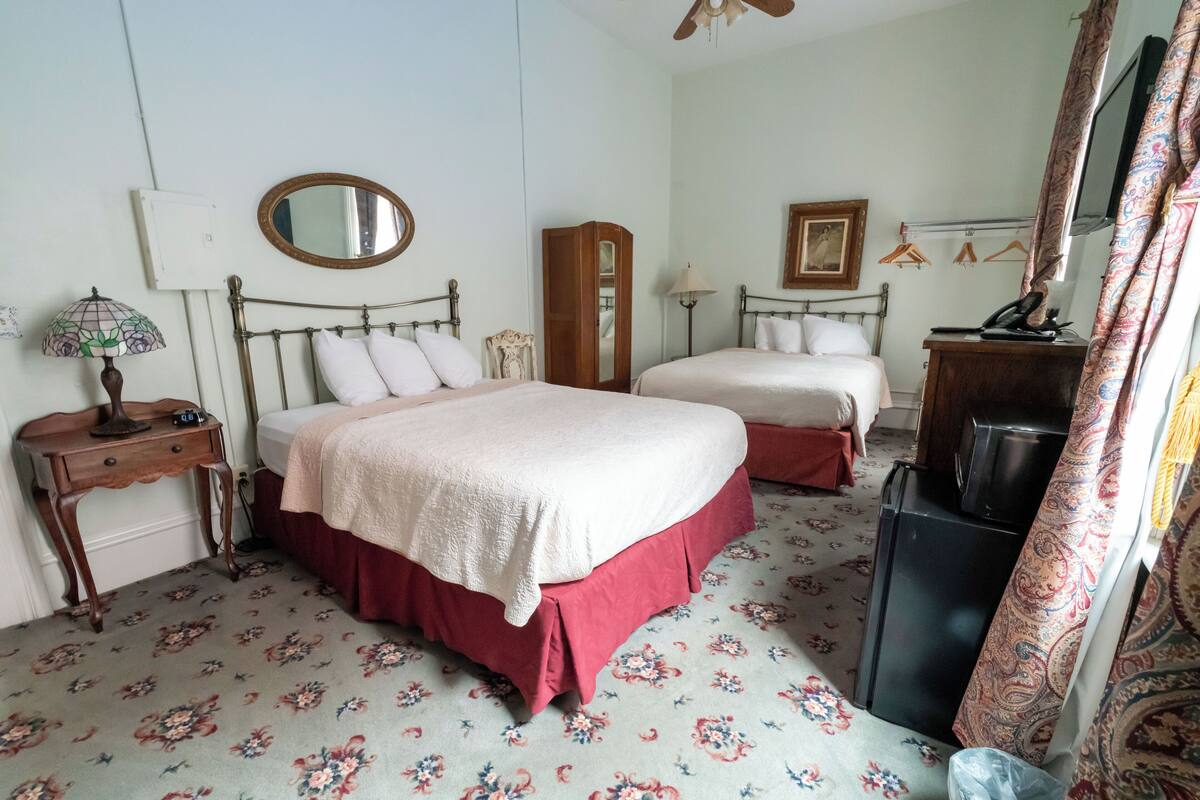 A bedroom with two beds, a dresser, a mirror, a lamp, and a television.