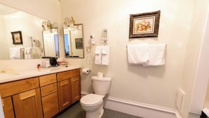 A bathroom with a white toilet, wooden cabinets, a large mirror, and a framed picture on the wall.