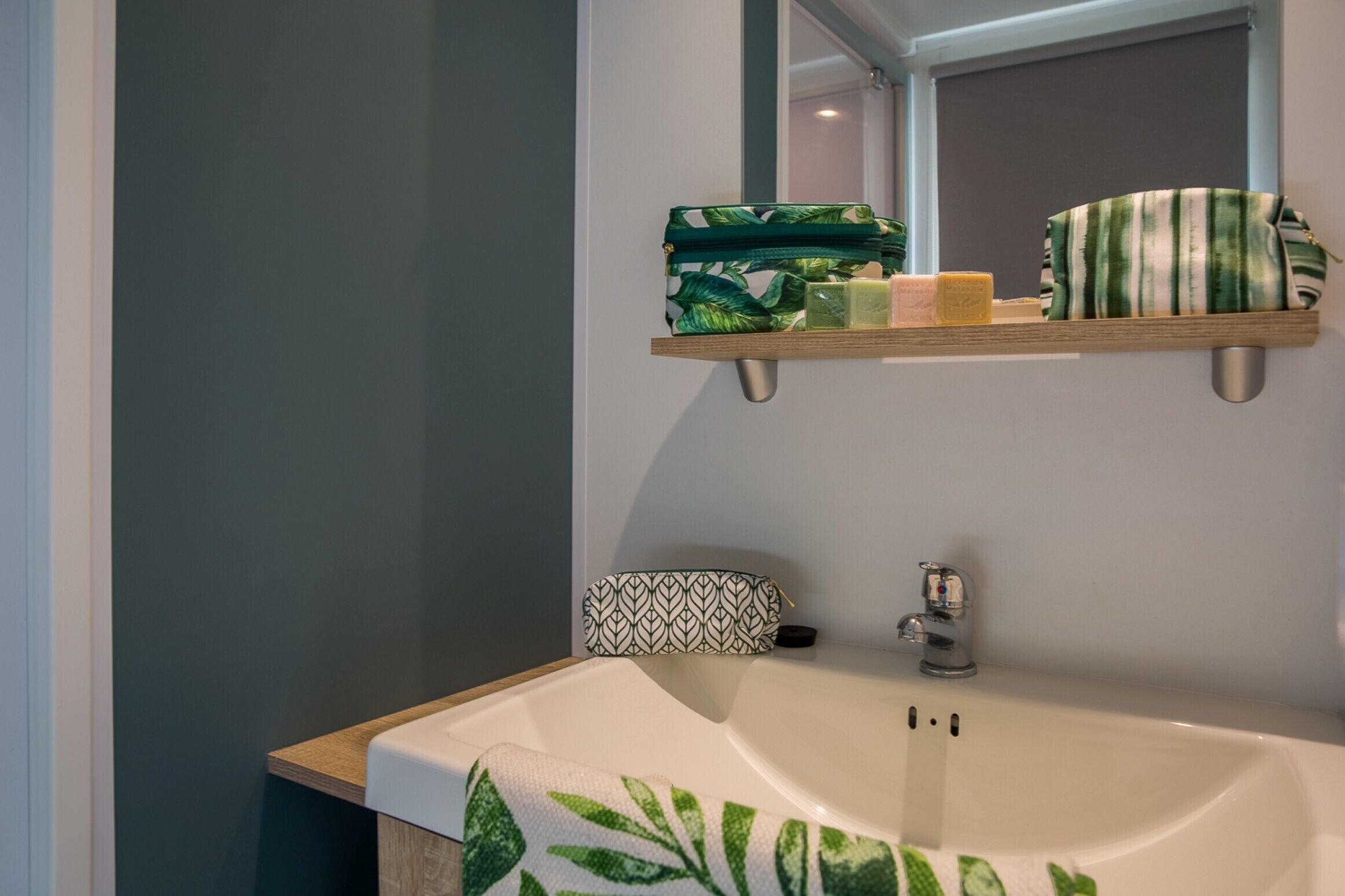 Een badkamer met een wit wastafelmeubel, een spiegel erboven en een plank met toiletartikelen.