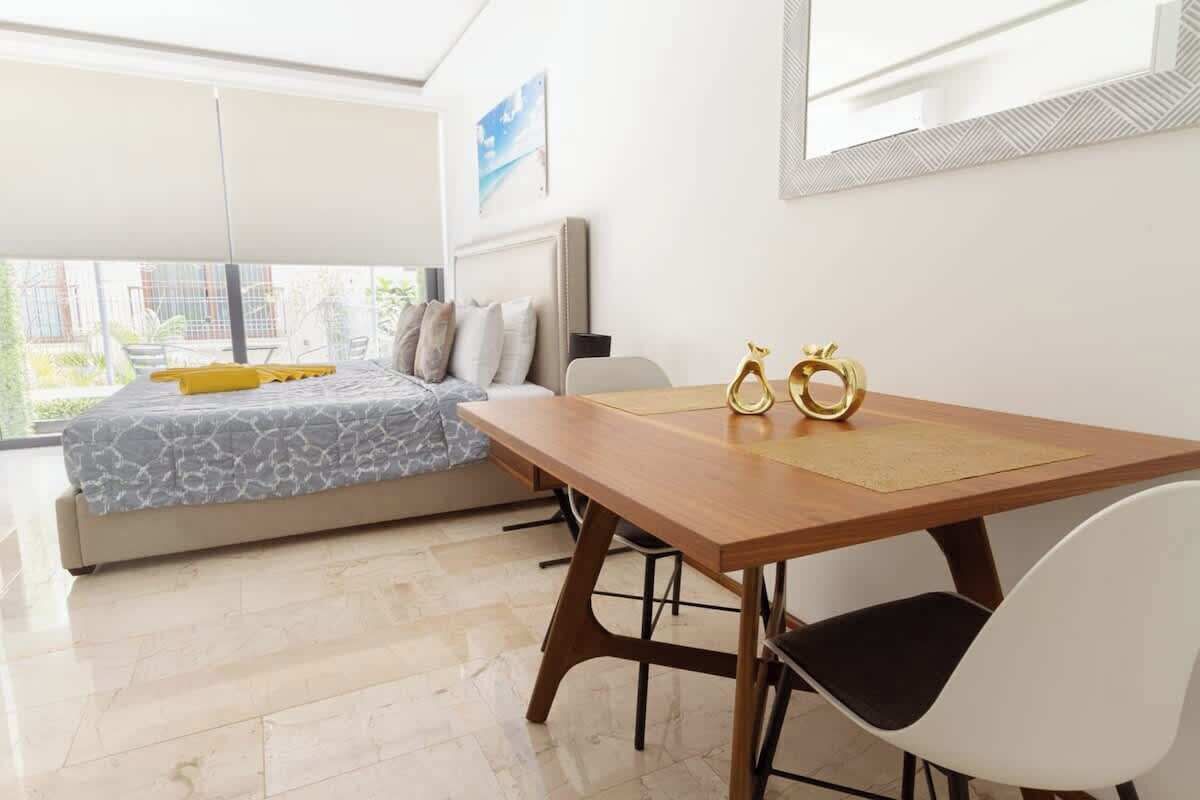 Una habitació moderna amb llit, taula de menjador i cadires, i un finestra gran.