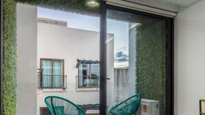 A modern bedroom with a large bed, a sliding glass door leading to a balcony, and two green chairs. - Modern Studio with Patio near 5th Avenue & Beach (Playa del Carmen)