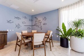 A dining area with a round wooden table and chairs, a wall with geometric wall art, and potted plants. - Studio w Rooftop Ocean Views Near Beach (Playa del Carmen)