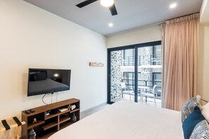 A modern hotel room with a large bed, a flat-screen TV, a wooden TV stand, and a balcony with a patterned view. - Studio w Rooftop Ocean Views Near Beach (Playa del Carmen)