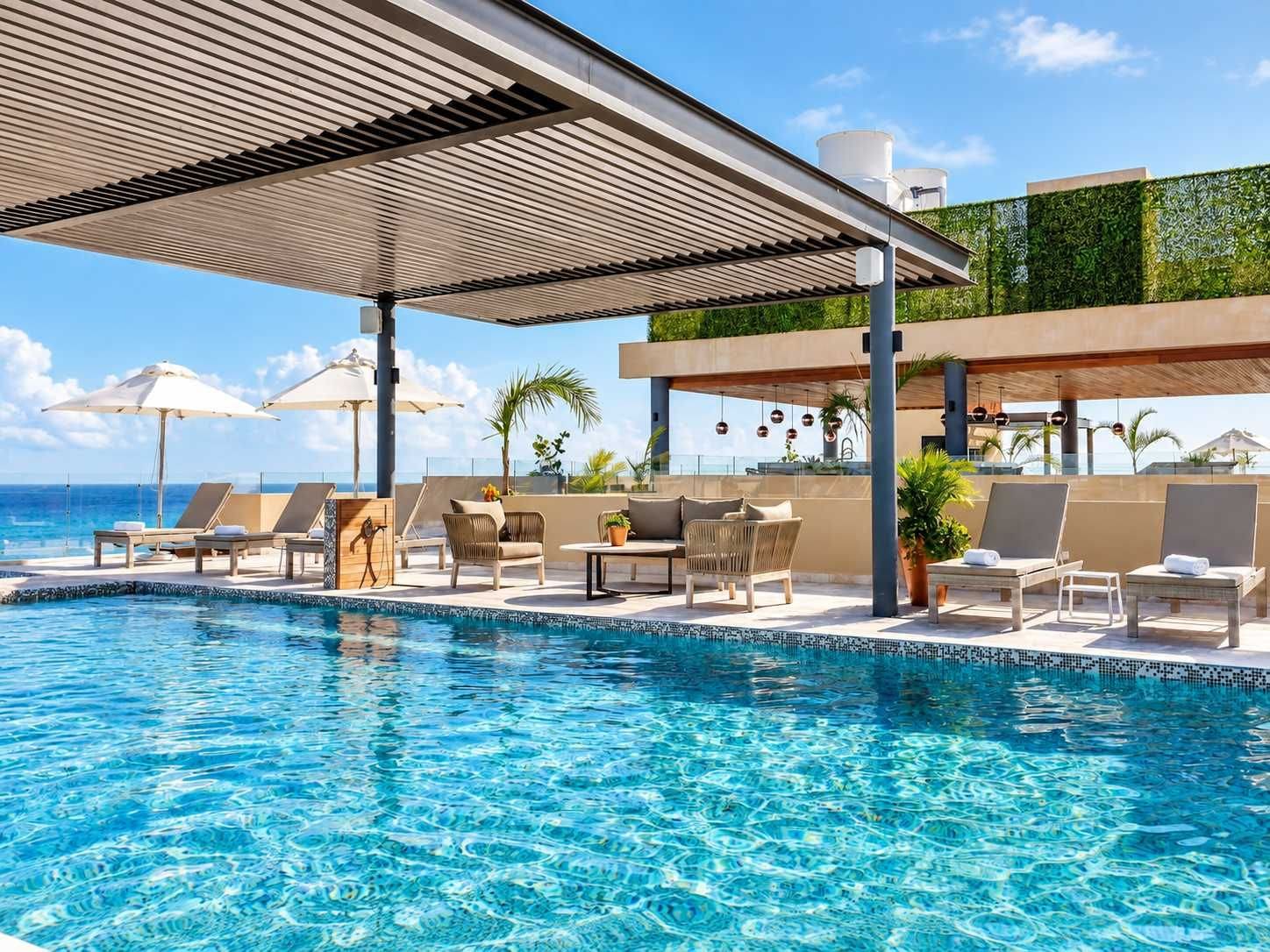 Un espace aménagé au bord de la piscine, avec des chaises longues, des parasols et une vue sur l’océan.