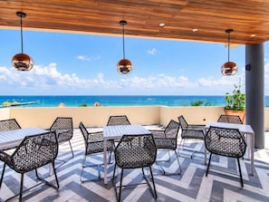 An outdoor seating area with tables and chairs, overlooking a coastal view. - 1BR in Singular Joy, best location in town (Playa del Carmen)