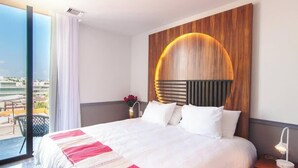 Moderni hotellihuone, jossa on suuri sänky, näköala kaupunkiin ja yksi seinä on koristeltu puupaneloinnilla.