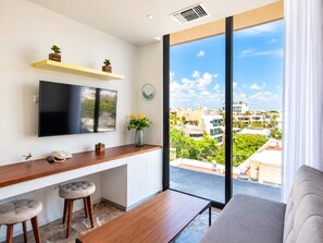 Ein modernes Wohnzimmer mit großem Fenster, Flachbildfernseher, Holztisch, zwei Barhocker und einer Couch.