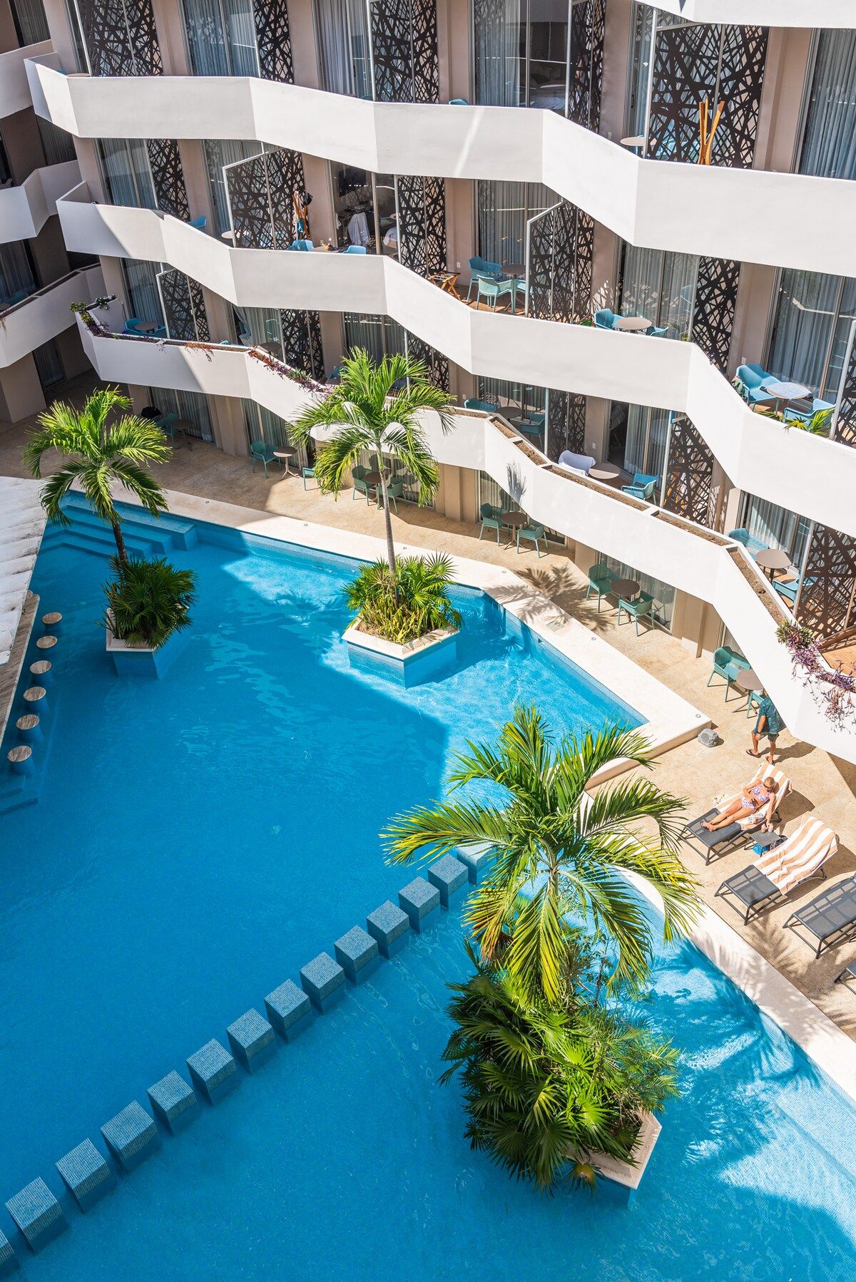A multi-level pool area with clear blue water, surrounded by lounge chairs and potted plants.