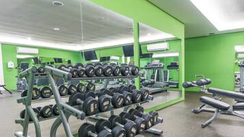 Un gimnasio con equipo de levantamiento de pesas, espejos y paredes verdes.