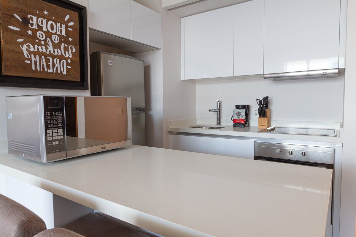 Cocina moderna con armarios blancos, microondas integrado, cafetera y bloque para cuchillos.