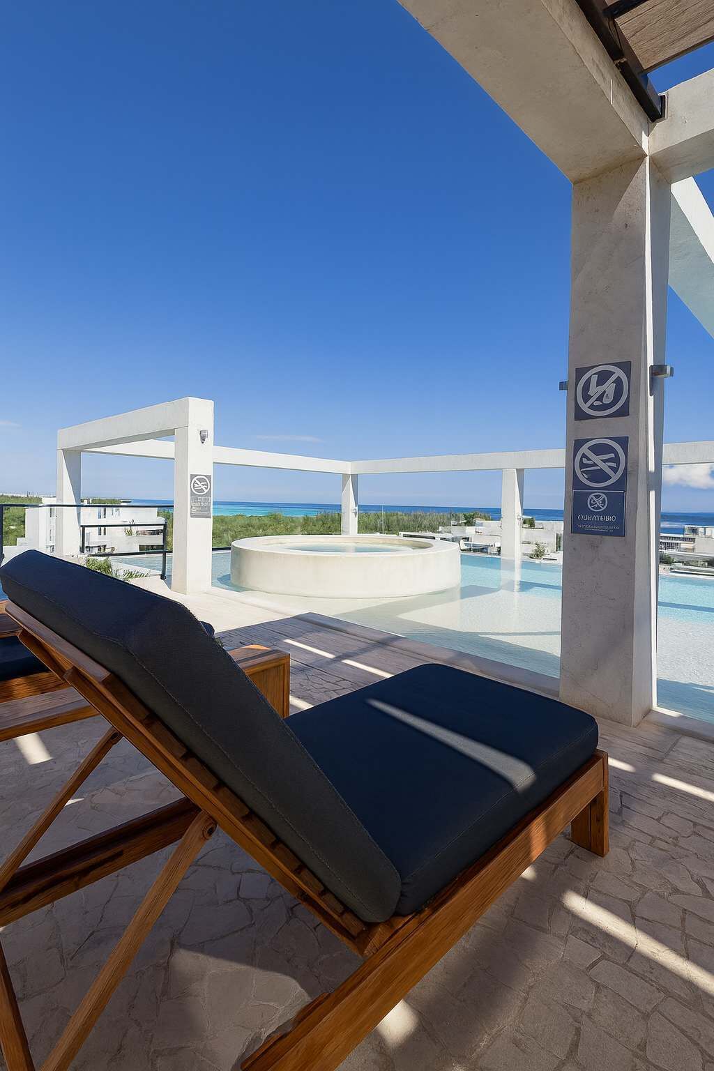 A poolside area with lounge chairs, a clear view of the sea, and a no swimming sign.
