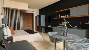 A modern living room with a sofa, a dining table with chairs, and a kitchen area with built-in shelves. - Modern Studio Steps from Beach w/ Rooftop Pool (Playa del Carmen)