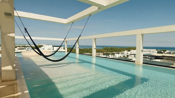 A rooftop pool with clear blue water, white beams, and a view of the ocean. - Modern Studio Steps from Beach w/ Rooftop Pool (Playa del Carmen)