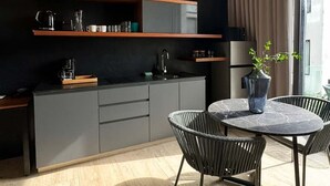 A modern kitchen with grey cabinets, a wooden shelf, and a dining area with a round table and chairs. - Modern Studio Steps from Beach w/ Rooftop Pool (Playa del Carmen)
