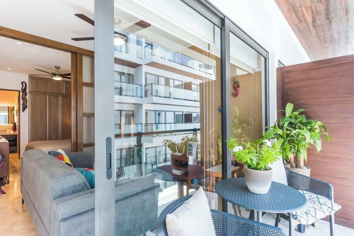 A modern living room with a sofa, a dining table with chairs, and a balcony with potted plants.