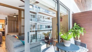 A modern living room with a sofa, a dining table with chairs, and a balcony with potted plants. - Central 1BR Condo w Rooftop Pools and Ocean View (Playa del Carmen)