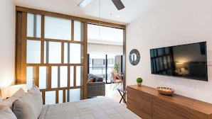 A modern bedroom with a bed, wooden headboard, a TV, and a sliding door leading to a balcony. - Central 1BR Condo w Rooftop Pools and Ocean View (Playa del Carmen)