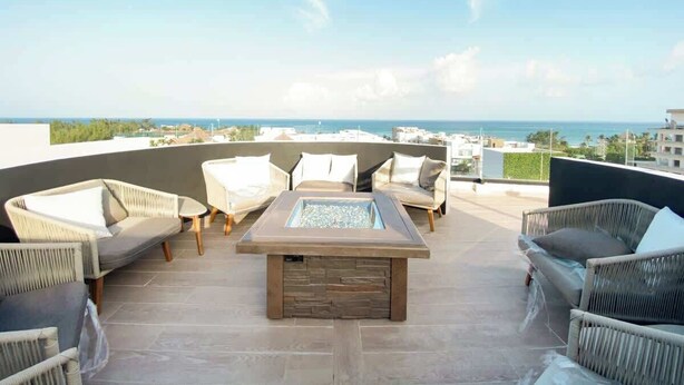 A rooftop terrace with wicker furniture, a central fire feature, and a view of the ocean. - Beach 1BR w Balcony, Washer & Rooftop Pool (Playa del Carmen)