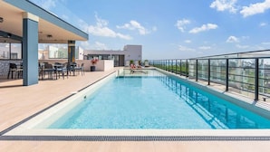A rooftop pool with clear blue water, surrounded by a glass railing, and a seating area with chairs and tables. - Beach 1BR w Balcony, Washer & Rooftop Pool (Playa del Carmen)