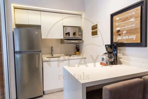 A modern kitchen with a built-in microwave, stainless steel refrigerator, and a coffee machine on the counter. - Rooftop Pool & Private Balcony Steps from Beach (Playa del Carmen)