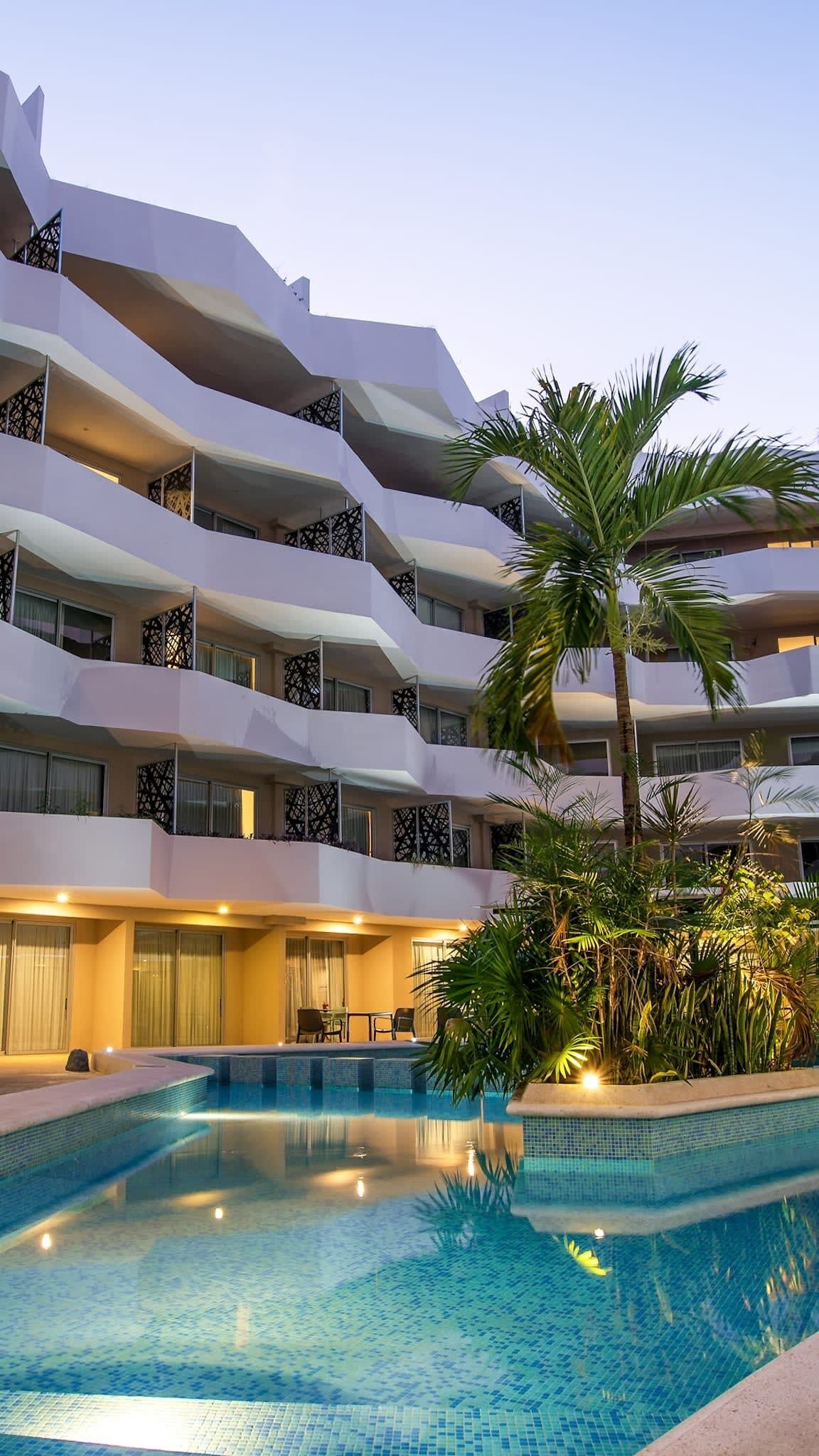 A multi-story hotel with a swimming pool, balconies, and tropical plants.