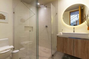 Een moderne badkamer met een douchecabine van glas, een houten wastafelmeubel en een ronde spiegel.