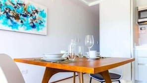 A dining area with a wooden table set for two, a white chair, and a blue abstract painting on the wall. - Oceanview Studio w/ Rooftop Pool Steps to Beach (Playa del Carmen)