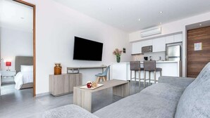 Een moderne woonkamer met een grijze bank, een houten salontafel en een flatscreen televisie aan de muur.