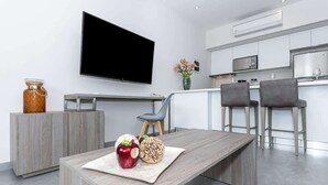 Een moderne keuken met een flatscreen televisie, een eethoek met een houten tafel en twee barkrukken.