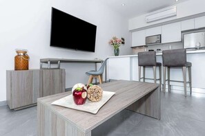 A modern kitchen with a flat-screen TV, a dining area with a wooden table, and two bar stools. - Stylish Condo w Rooftop Pool & Gym Near 5th Ave (Playa del Carmen)
